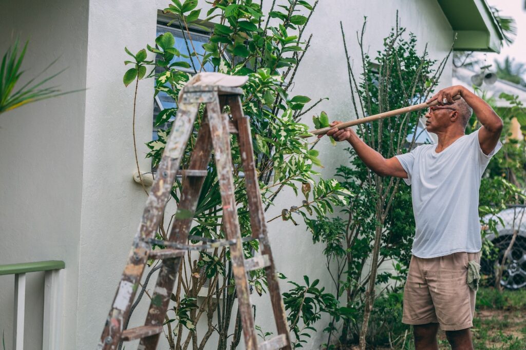 man in a white shirt painting the exterior of his home because painting your walls it's a great way to boost your home's curb appeal.