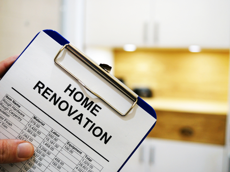 Image shows someone holding a blue clipboard with the words home renovations  on top of it with a check list of goods.