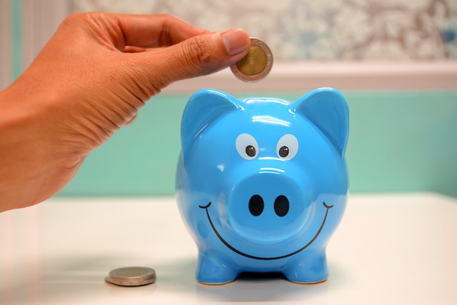 A person putting money in a blue piggy bank depicting home remodels that make staying put a joy and cost effective.

