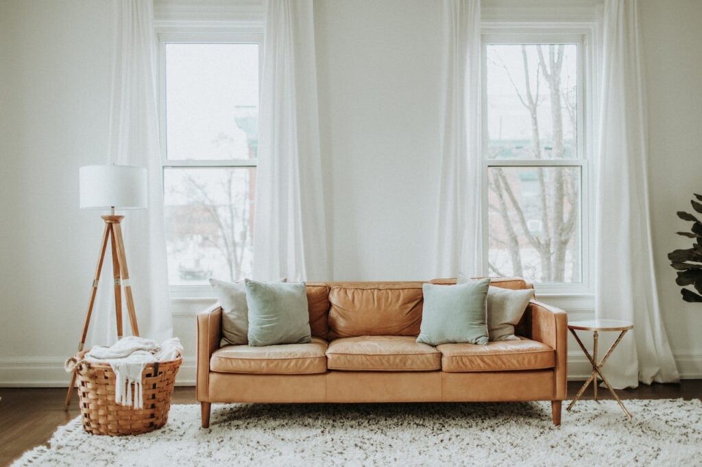 A Beige sofa, white curtains, lamp, and carpet