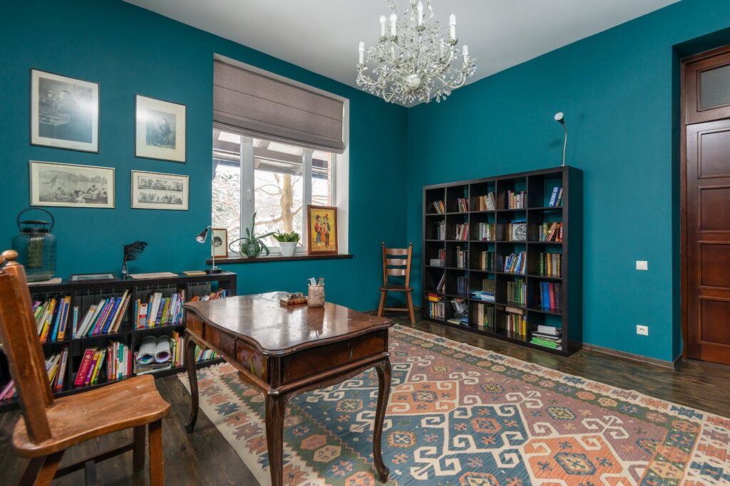 A study with bookshelves, a colorful carpet, and a chandelier
