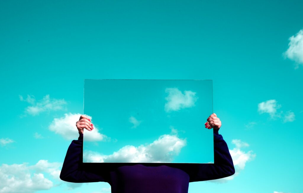 A man holding a mirror against the sky.