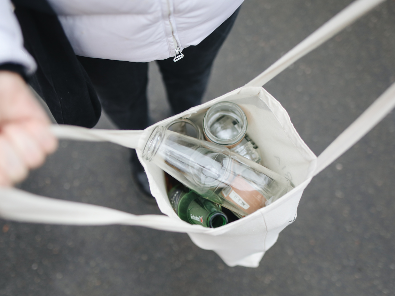 an image shows someone depicting Sustainable Living with cleaned used bottles in a cloth bag.